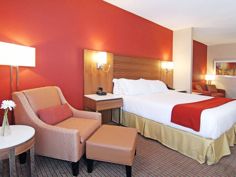 A hotel room with a bed, a chair, a bedside table, a lamp, and a painting on the wall.
