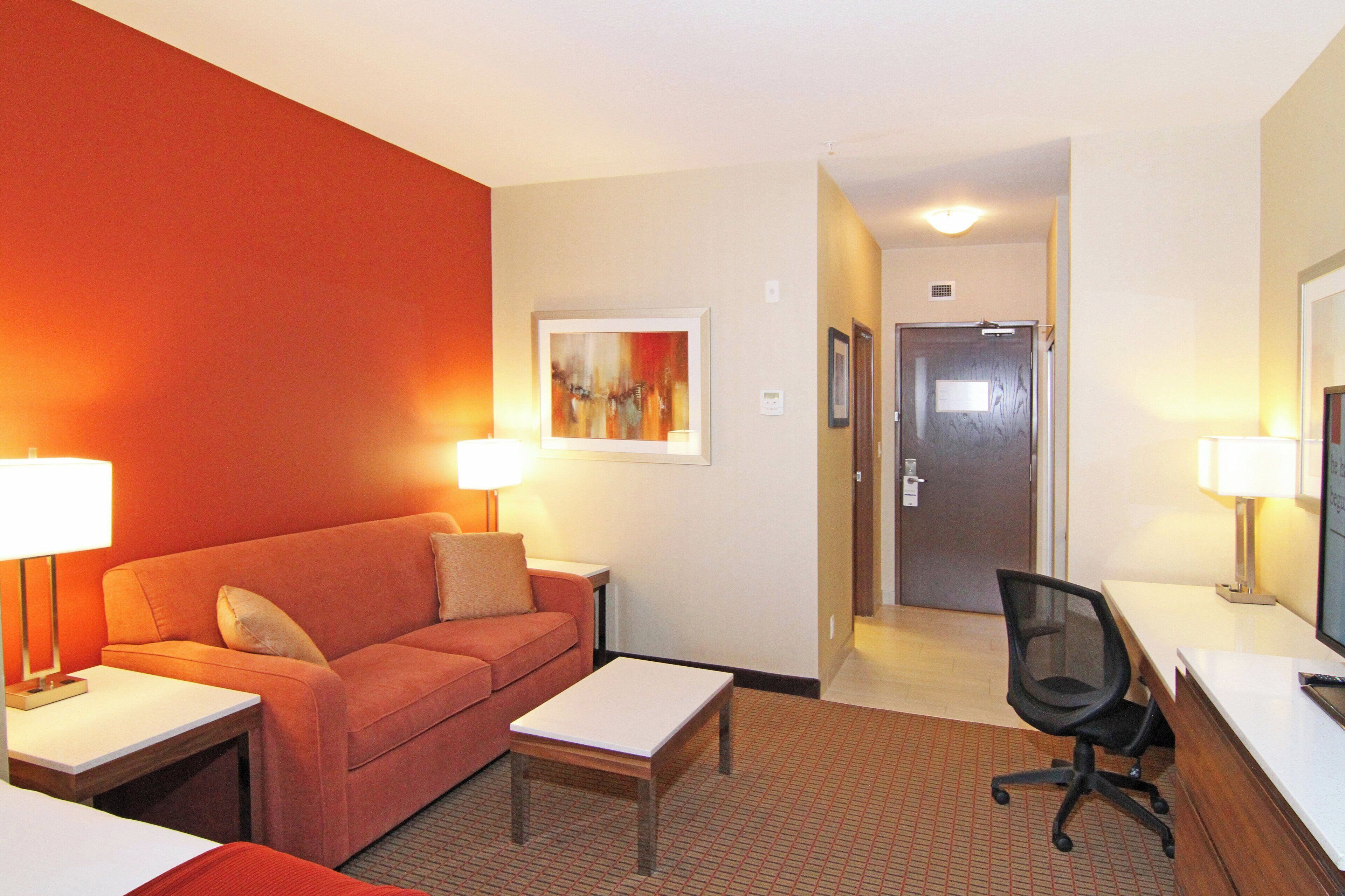 Ein Hotelzimmer mit einem roten Sofa, einem kleinen Tisch, einem Schreibtisch mit einem Computer und einem Stuhl.