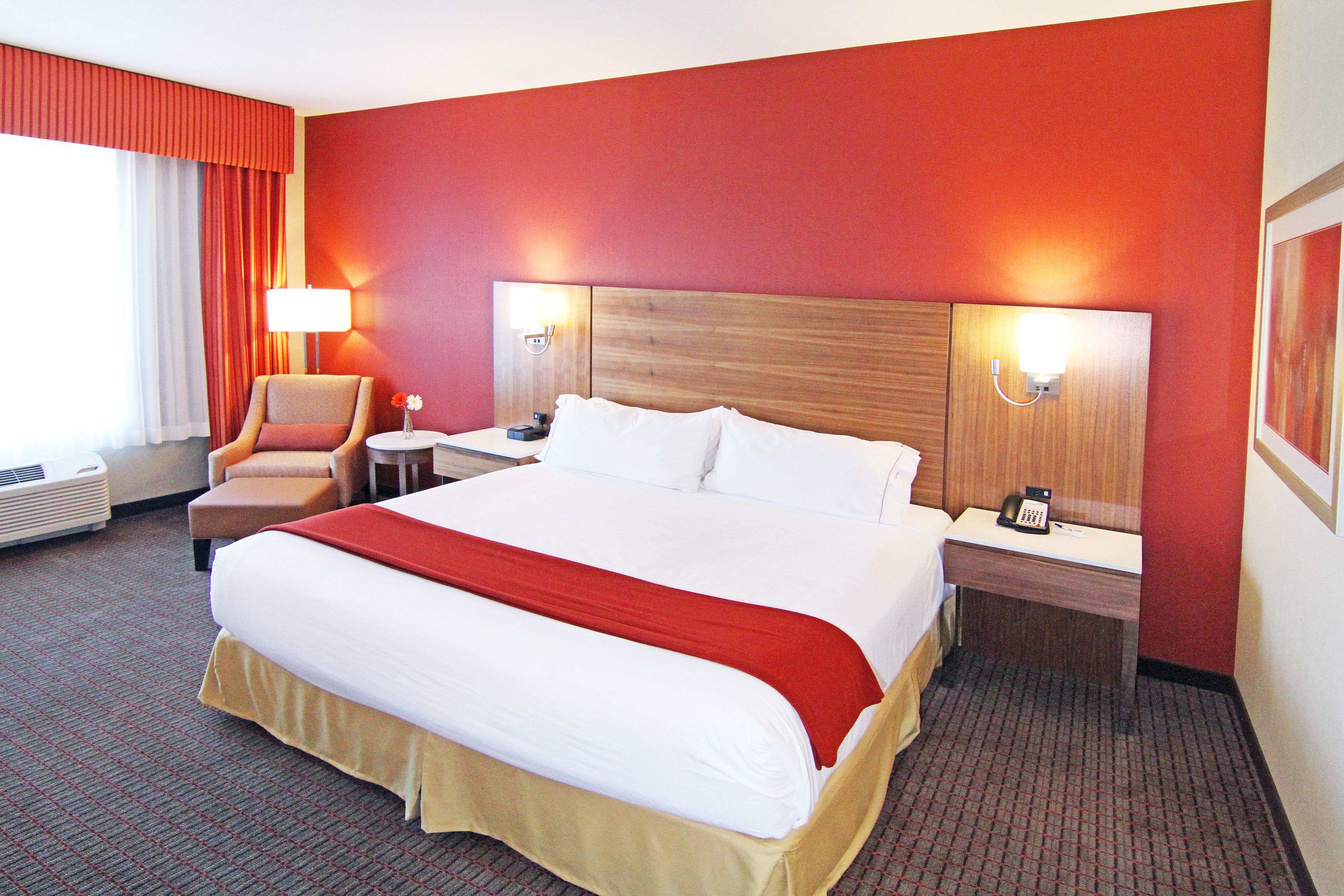 Habitación de hotel con una cama grande, dos mesitas de noche, una silla, una lámpara y un teléfono instalado en la pared.