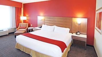 Habitación de hotel con una cama grande, dos mesitas de noche, una silla, una lámpara y un teléfono instalado en la pared.