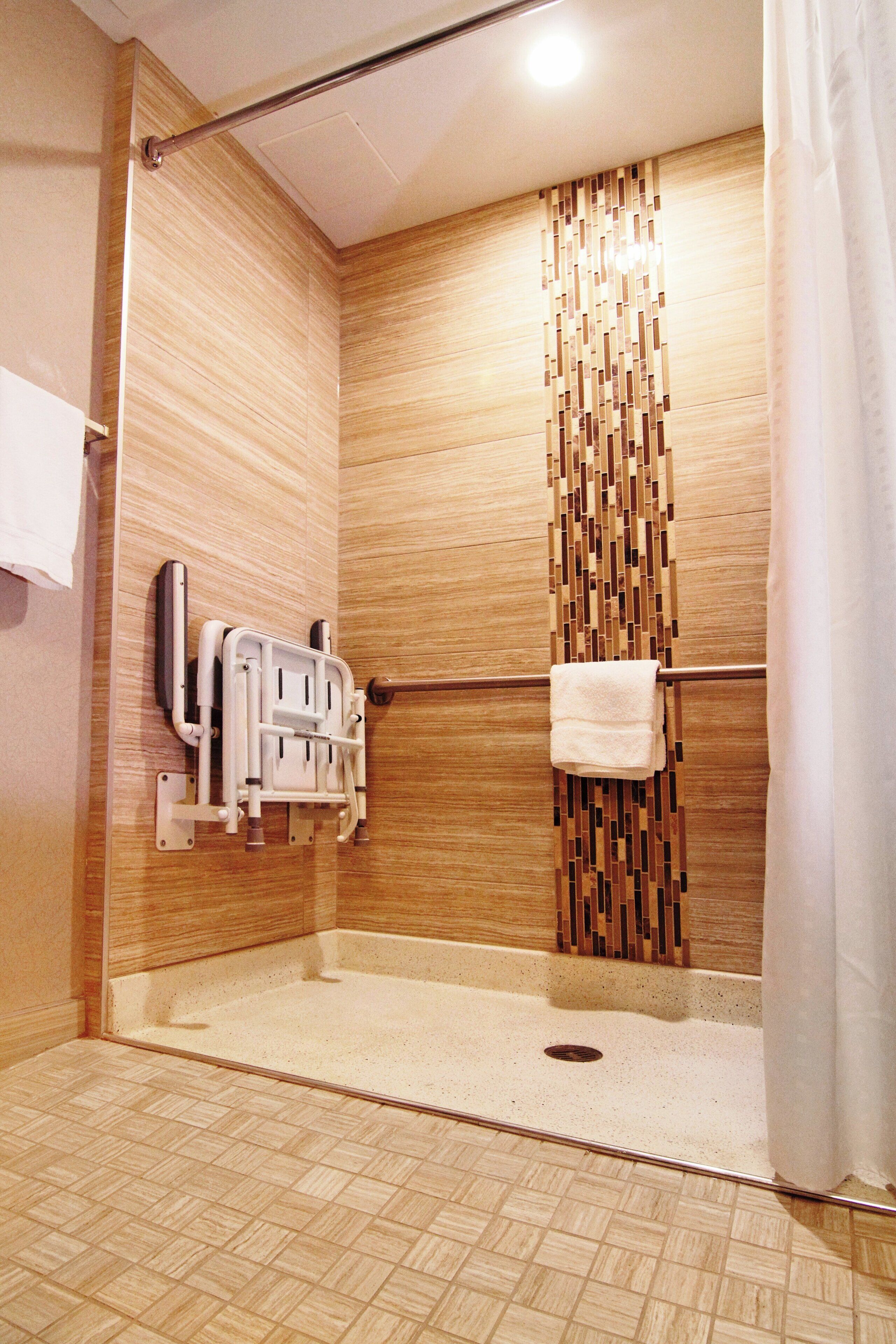 A shower with a grab bar, a towel rack, and a textured wall.