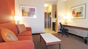A hotel room with a red sofa, a small table, a desk with a chair, and artwork on the walls.