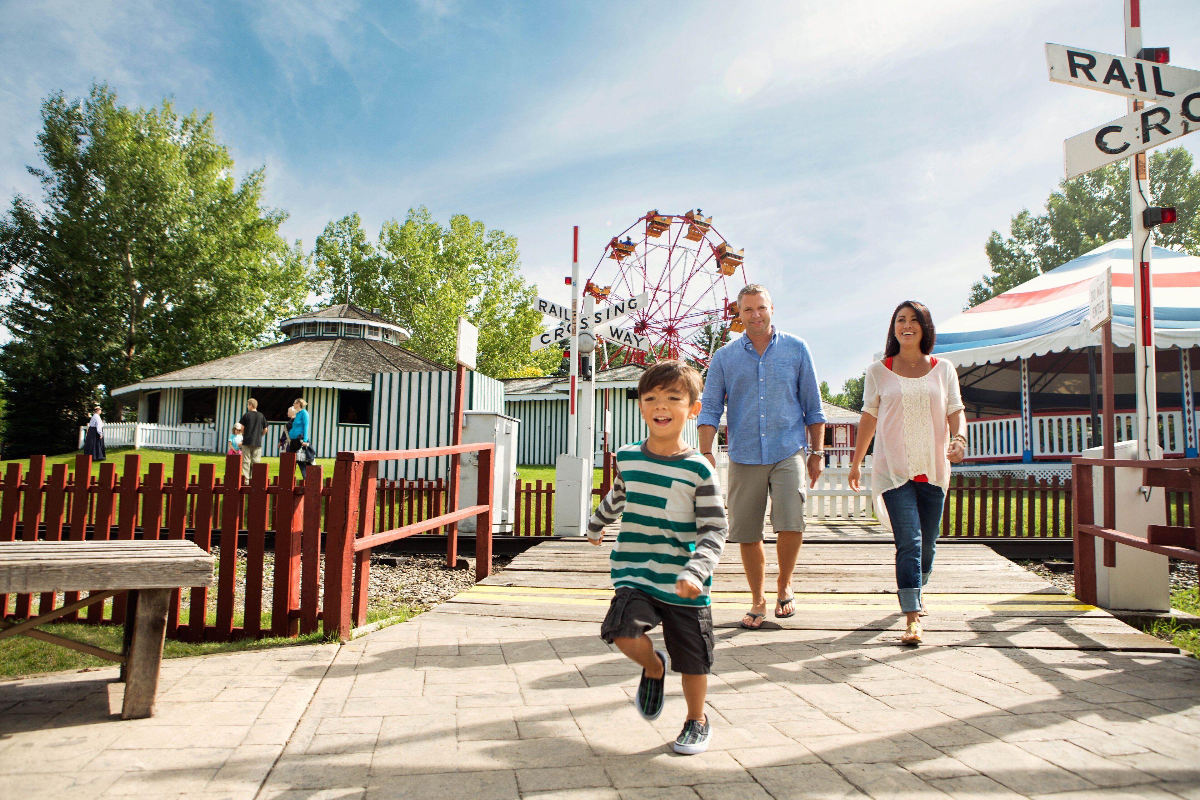 A family walking on a paved path at a park with a ferris wheel and a gazebo in the background.
