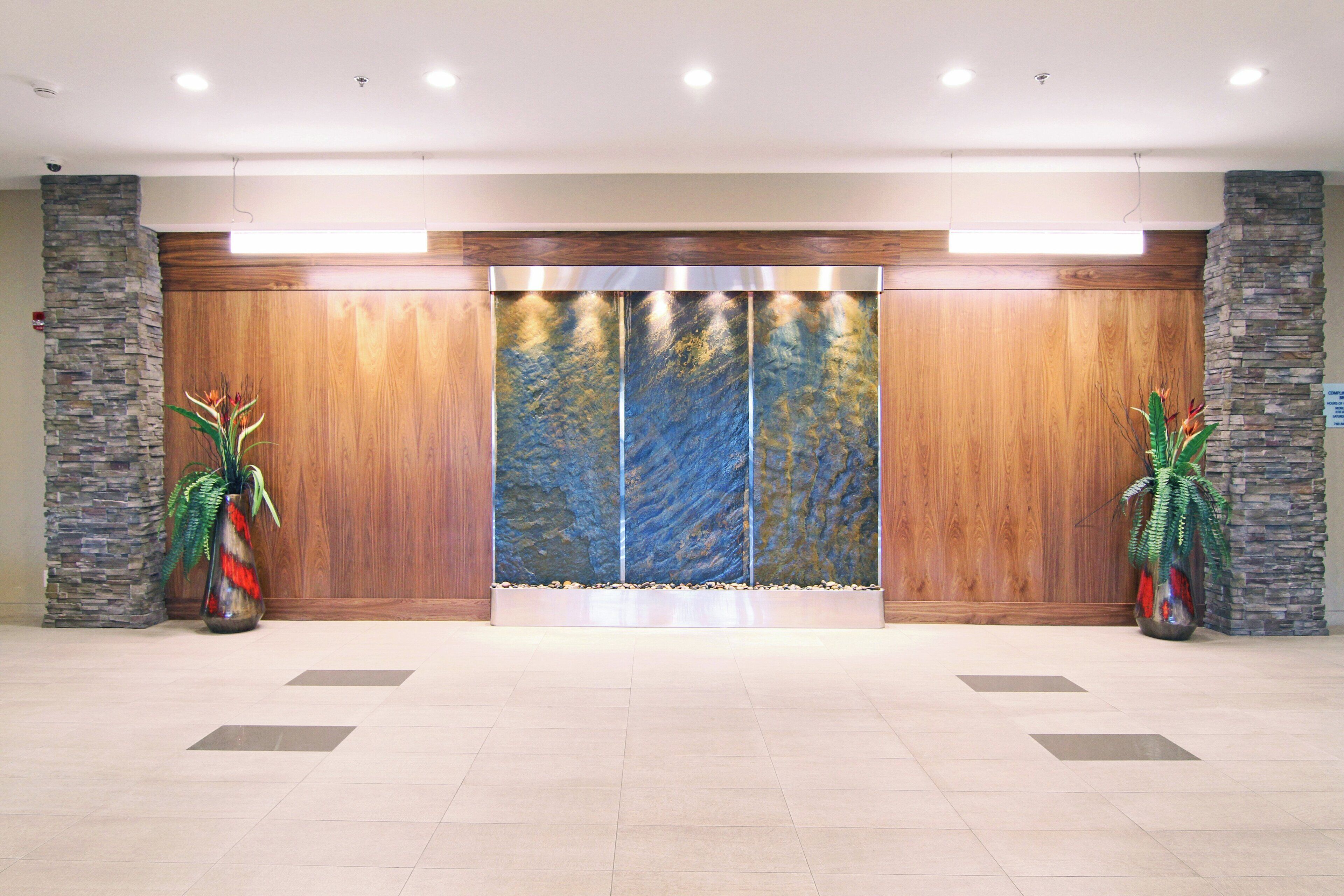 Zona de recepción con pared de piedra, paneles de madera y un gran panel decorativo. Hay dos plantas en macetas con follaje verde.