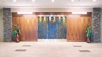 Zona de recepción con pared de piedra, paneles de madera y un gran panel decorativo. Hay dos plantas en macetas con follaje verde.