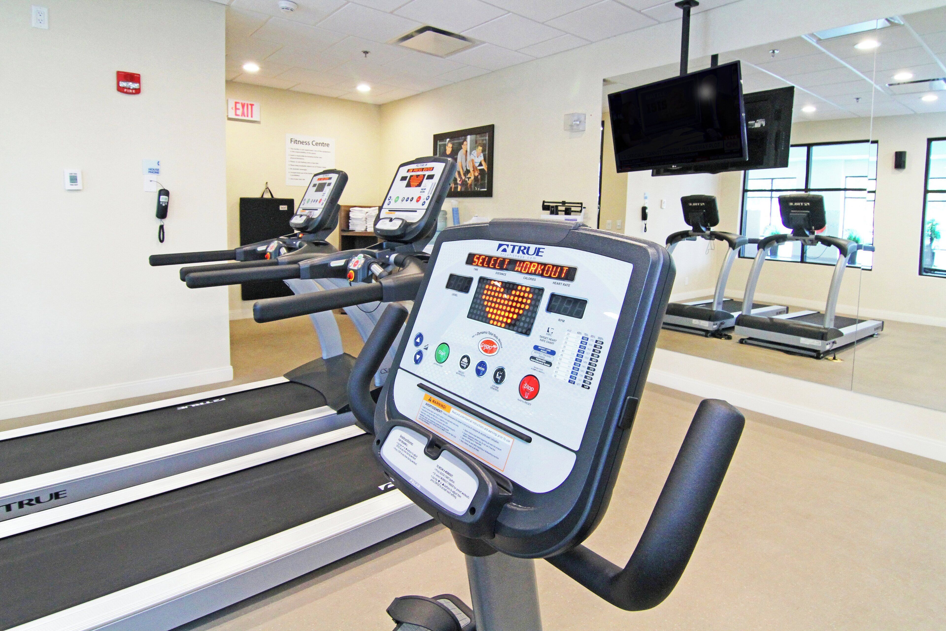 Een fitnessruimte met loopbanden, een digitaal scherm en een televisie aan de muur.