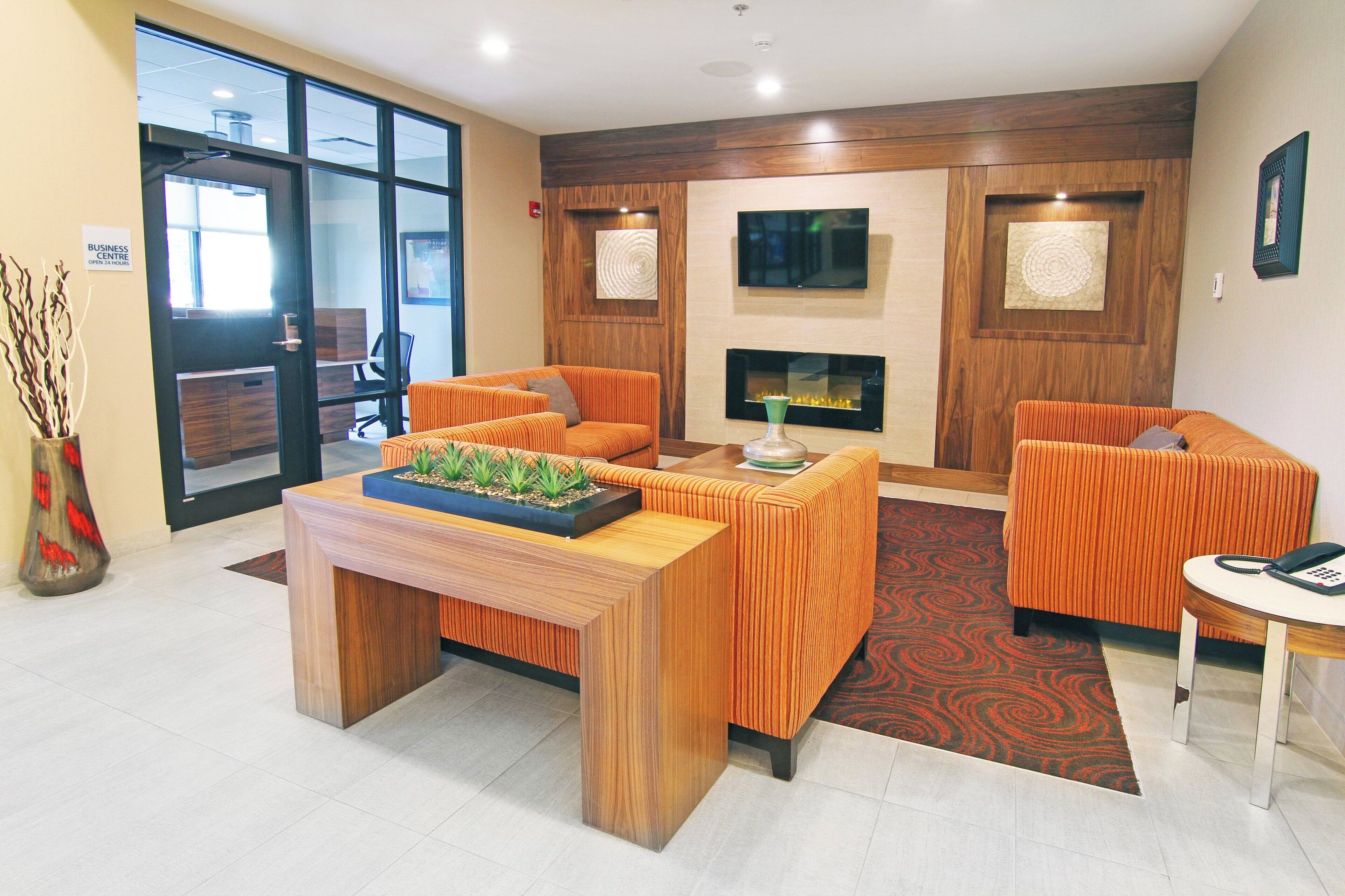 A reception area with a wooden reception desk, two sofas, a fireplace, and a television on the wall.