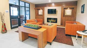 A reception area with a wooden reception desk, two sofas, a fireplace, and a television on the wall.