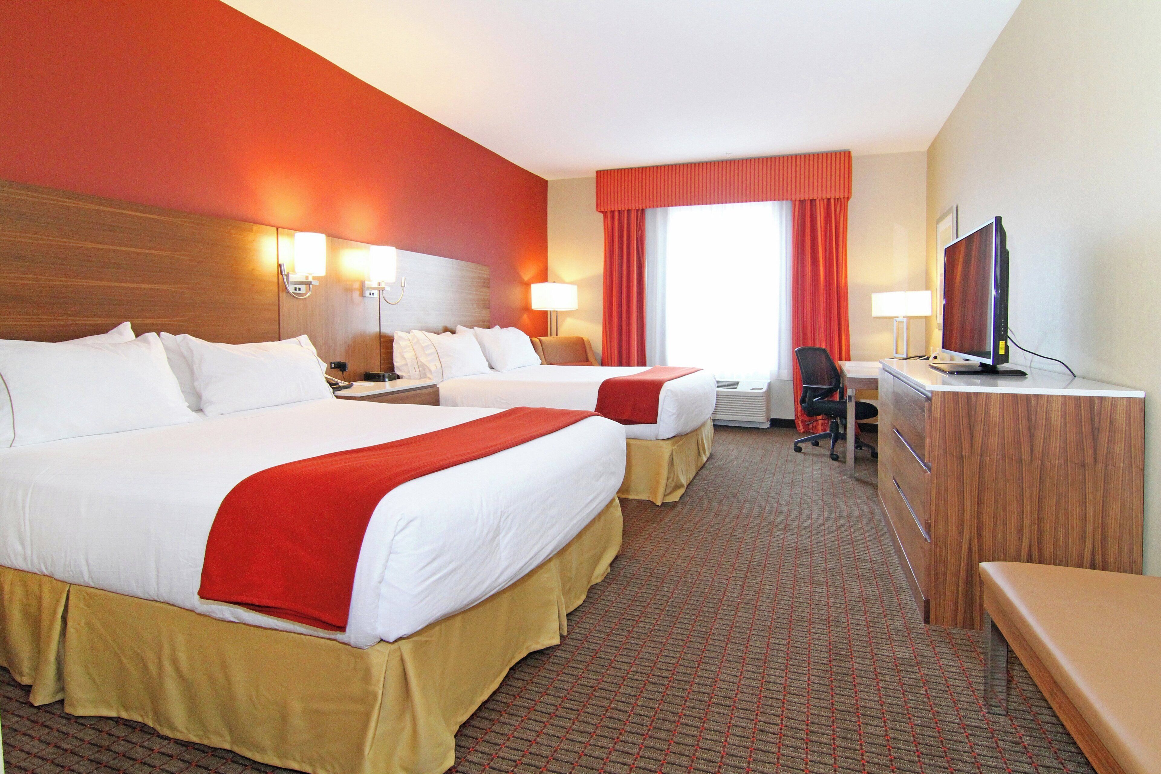 A hotel room with two beds, a desk, a television, and a window with curtains.