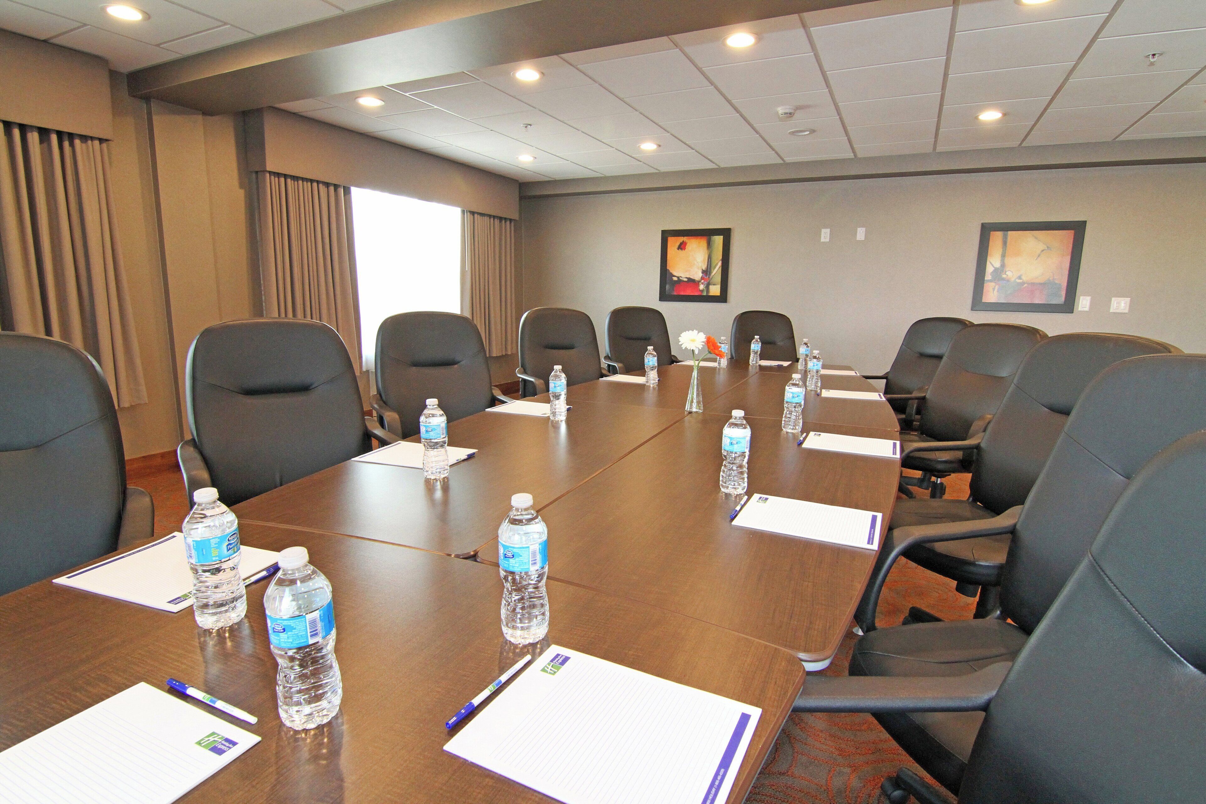 A conference room with a long table, multiple chairs, water bottles, pens, and notepads.