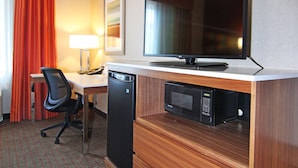 A compact hotel room with a wooden desk, a flat-screen TV, a microwave, and a compact dishwasher.