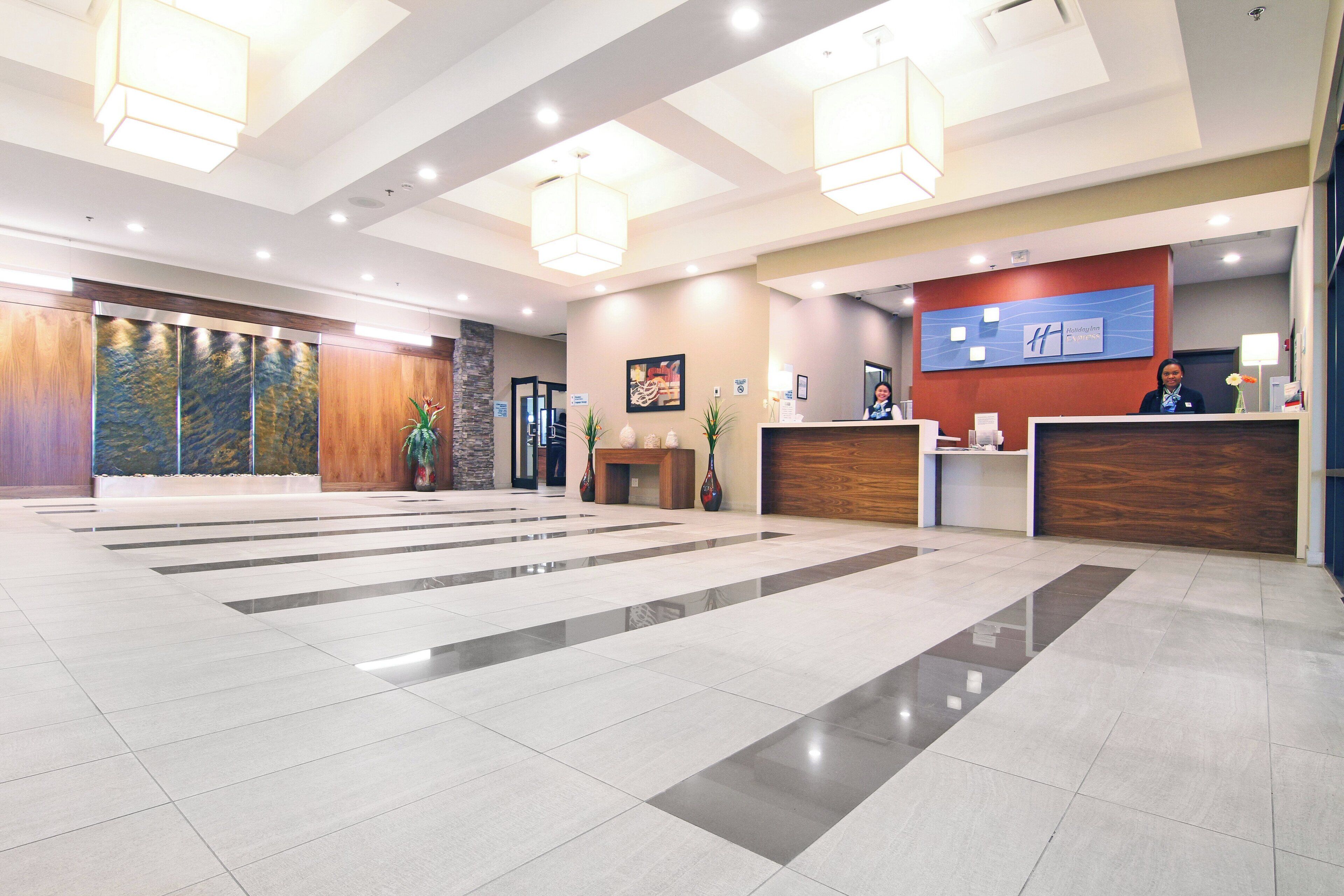 Uma área de recepção de hotel com design moderno, incluindo um balcão de atendimento, uma grande placa na parede e uma área de recepção com recepcionista.