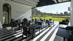 A modern outdoor dining area with black and white striped flooring, black tables and chairs, and a large glass wall offering a view of a green landscape. - HD Duecitânia Design Hotel (Penela)