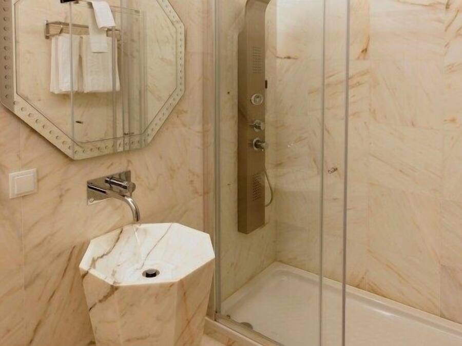 A bathroom with a hexagonal marble sink, a glass shower enclosure, and a large mirror with a towel rack.