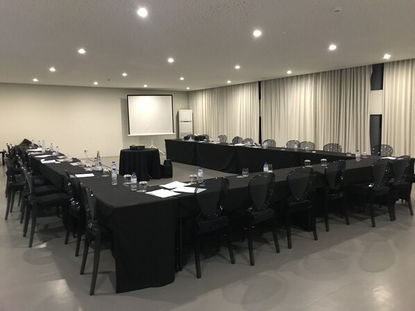 Un salón de conferencias con una larga mesa, sillas, una pantalla de proyector y una pizarra.