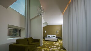 A modern hotel room with a green sofa, a white bed, and a chandelier. - HD Duecitânia Design Hotel (Penela)