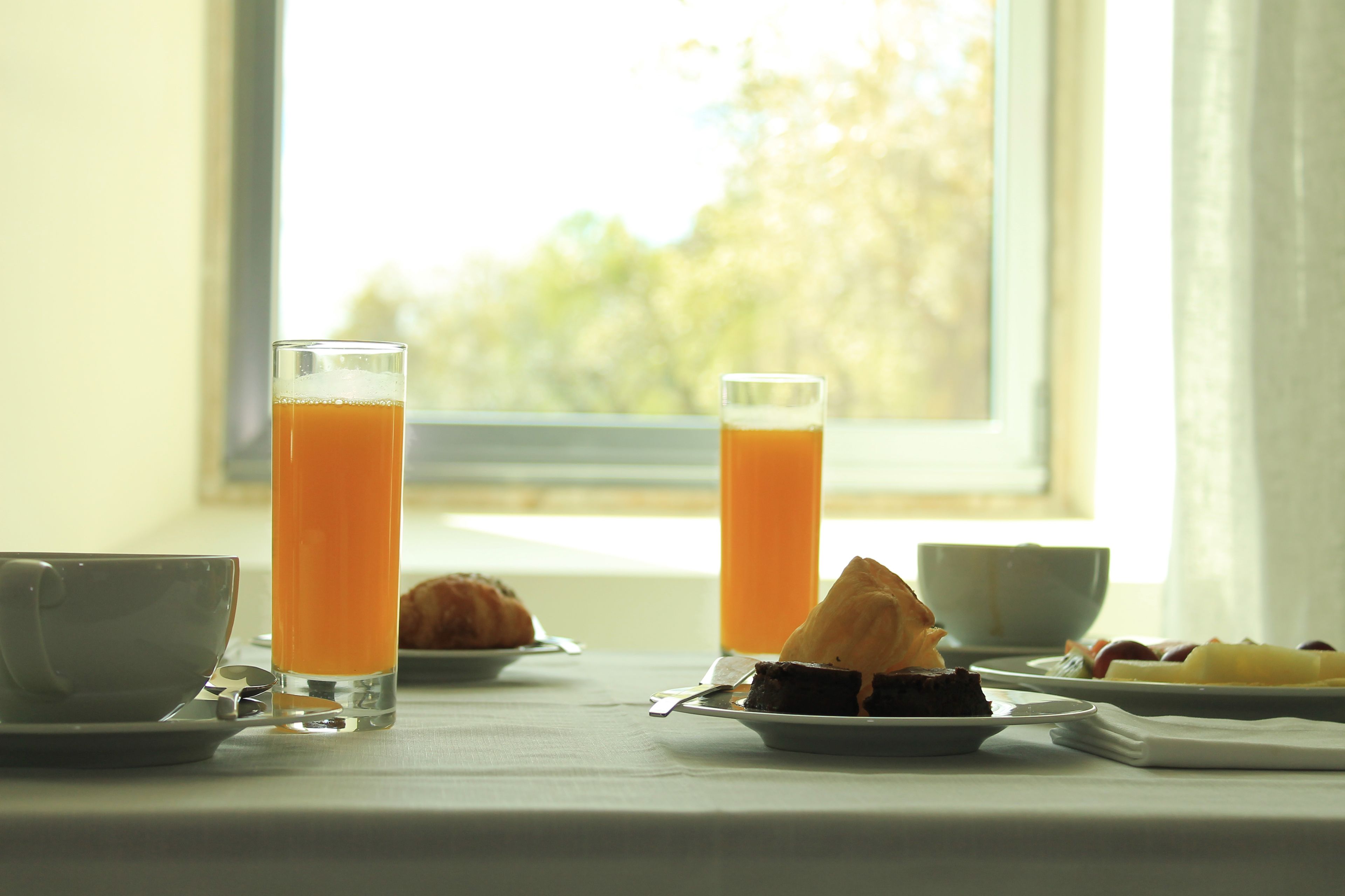 Una mesa de desayuno con un croissant, una porción de pastel y un vaso de jugo de naranja.