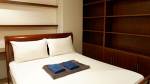 Una cama bien hecha con almohadas blancas y una manta gris, cabecera de madera y un amplio armario de madera.