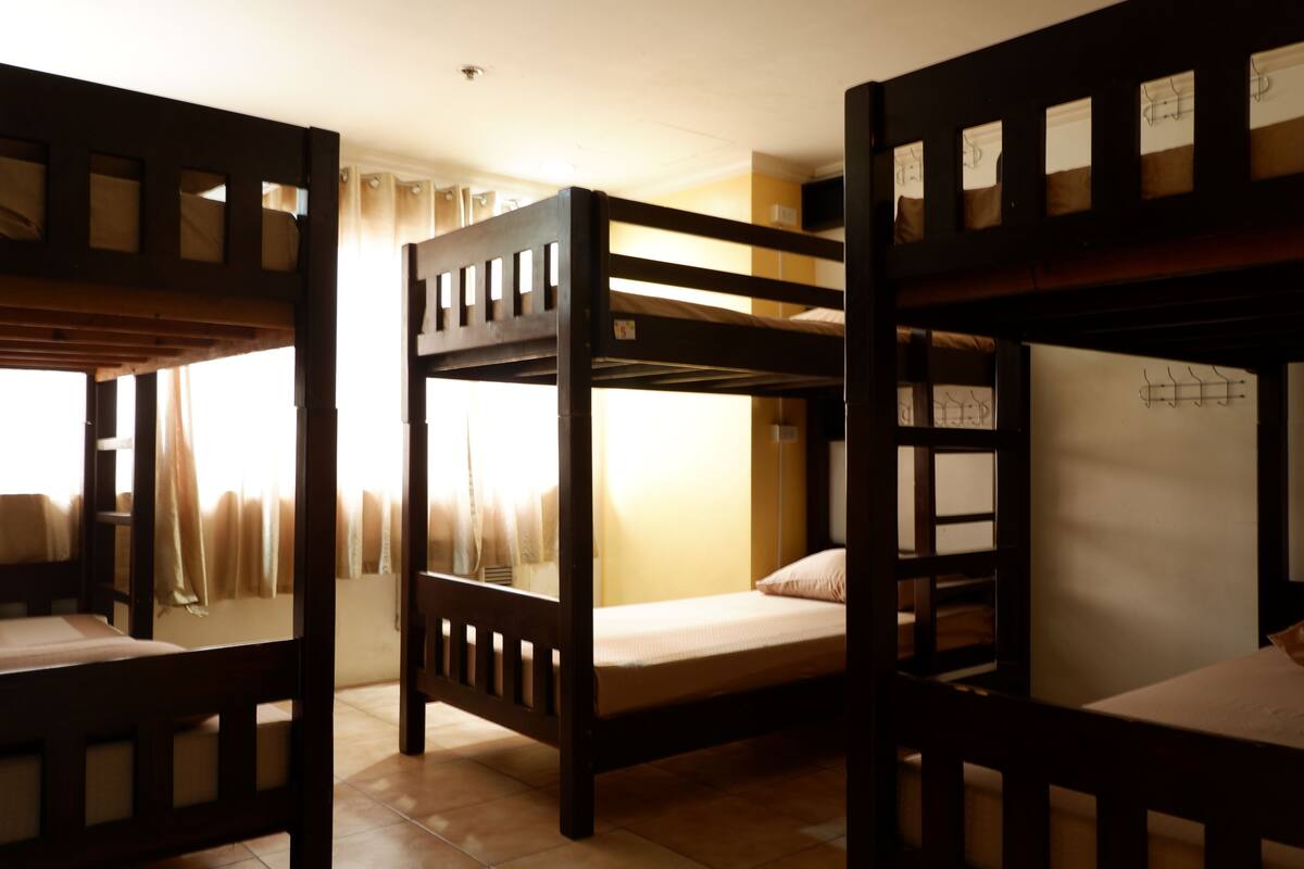 A dormitory room with bunk beds, a window with curtains, and a tiled floor.