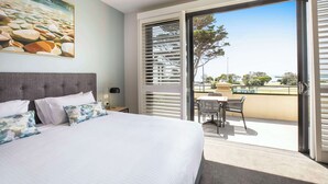 A bedroom with a large bed, a painting of rocks, a balcony with a table and chairs, and a view of the outdoors.