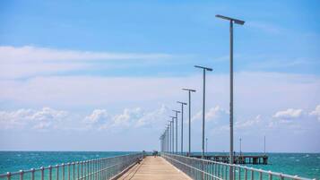 A long pier extending into the sea with railings and street lamps.