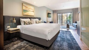 A modern bedroom with a large bed, a bedside table, a lamp, and a view of the outdoors through a glass door.