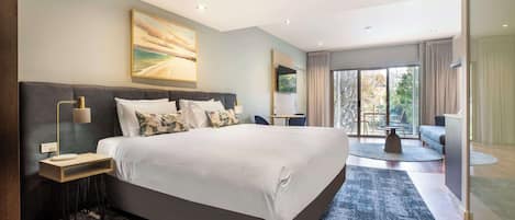 A modern bedroom with a large bed, a bedside table, a lamp, and a view of the outdoors through a glass door.