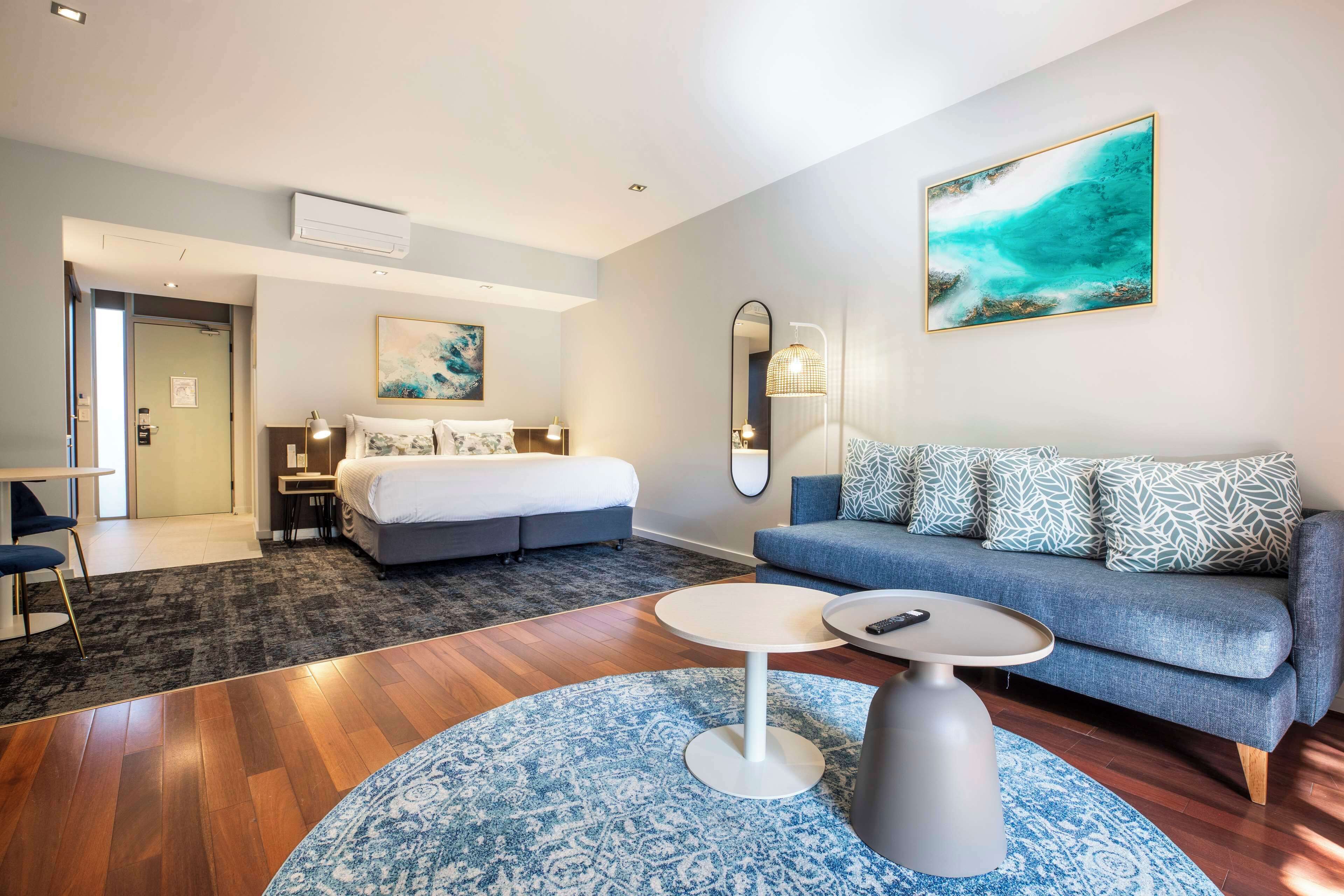 Una habitación de hotel con cama, sofá, mesa de comedor y mesa auxiliar.