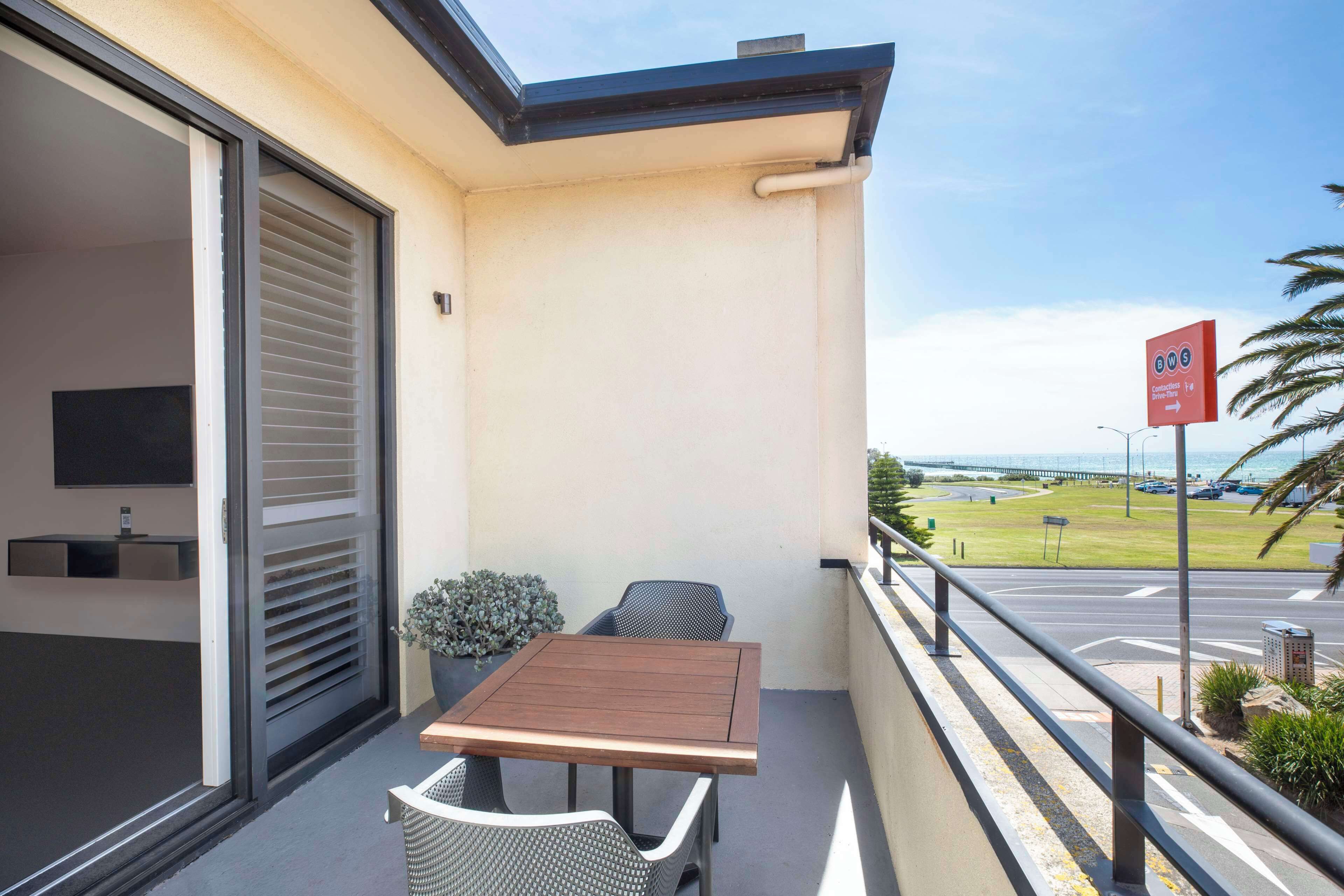 A balcony with a table and chairs, a sliding door, and a view of a road and greenery.