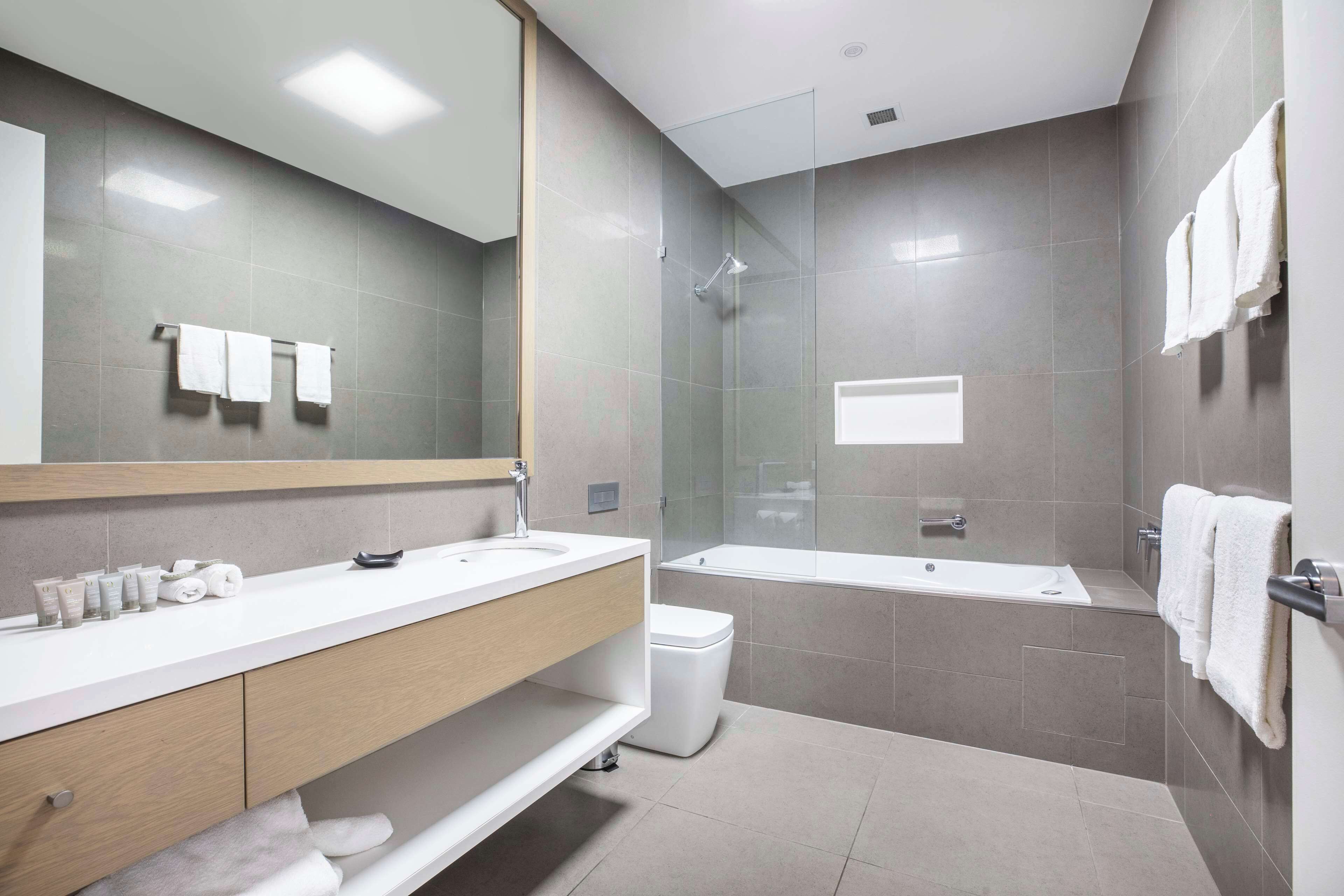 Une salle de bain moderne avec un grand miroir, un lavabo blanc, un meuble-vasque et une douche séparée par des parois en verre.