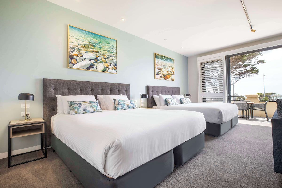 A hotel room with two beds, a small desk, and a balcony with a table and chairs.