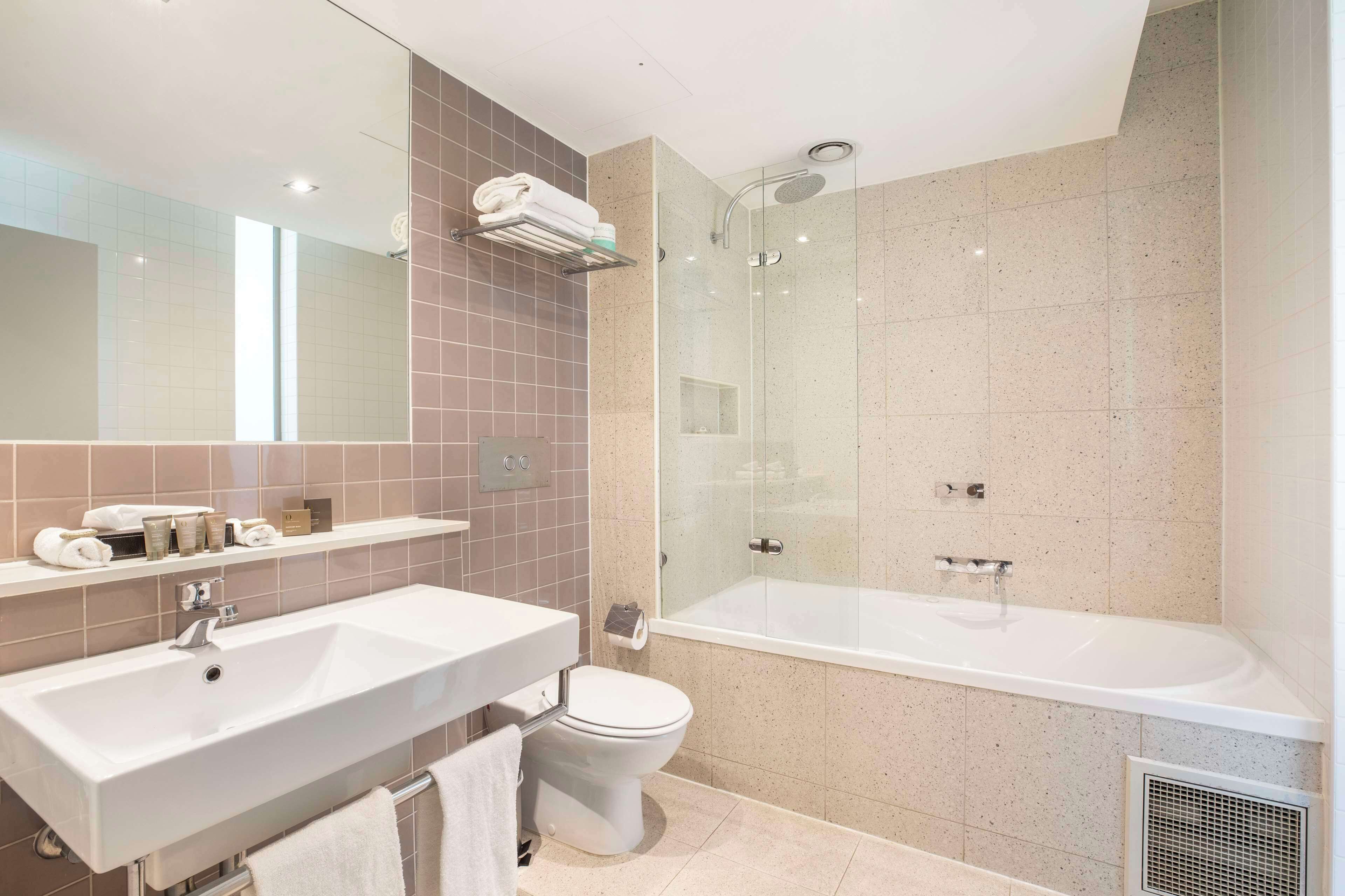 A modern bathroom with a double sink, toilet, and a glass-enclosed shower.