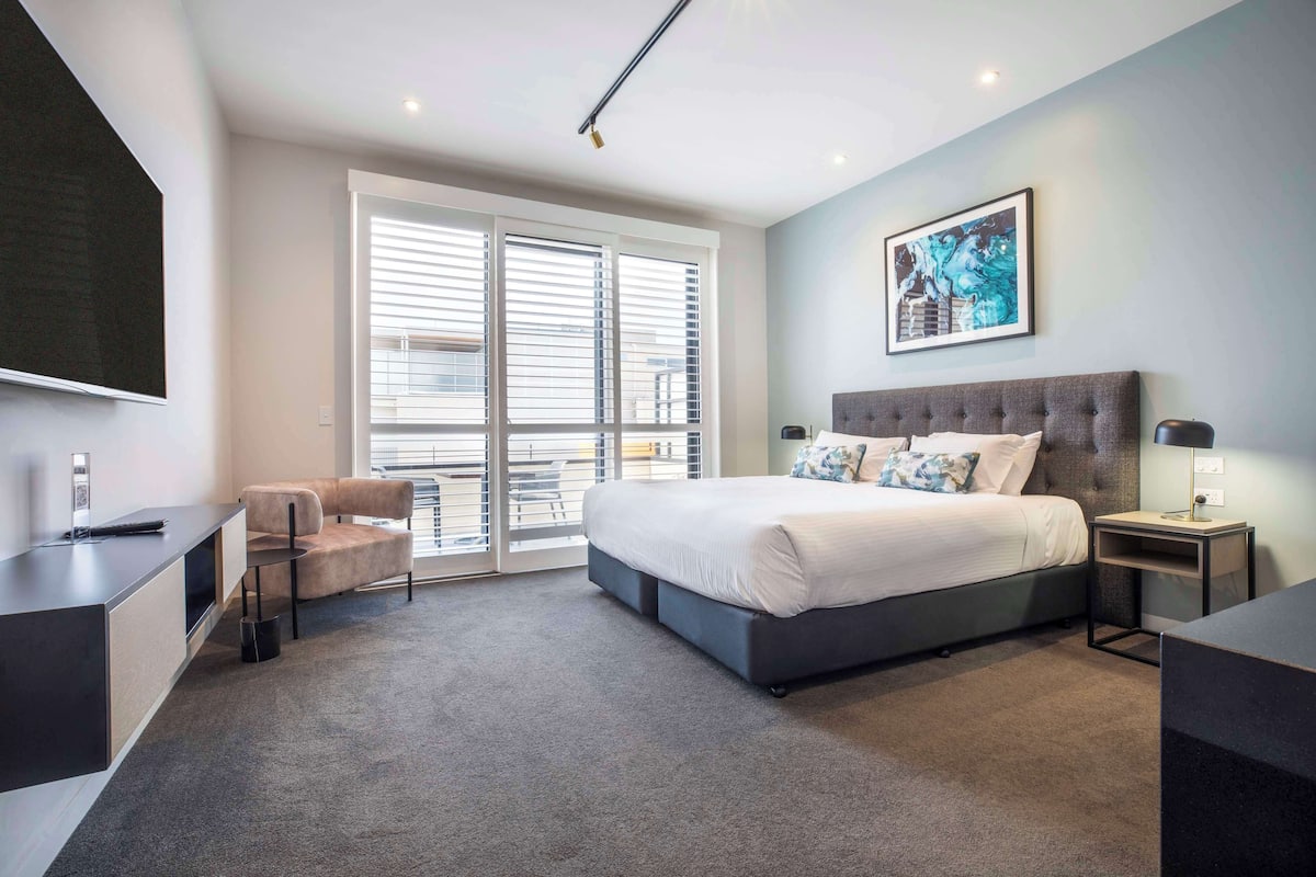 A modern bedroom with a large bed, a desk, a chair, and a TV.
