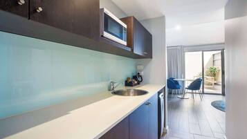 Una cocina moderna con microondas integrado, un lavamanos y armarios. Se observa un comedor con una mesa y sillas a través de una puerta de vidrio.