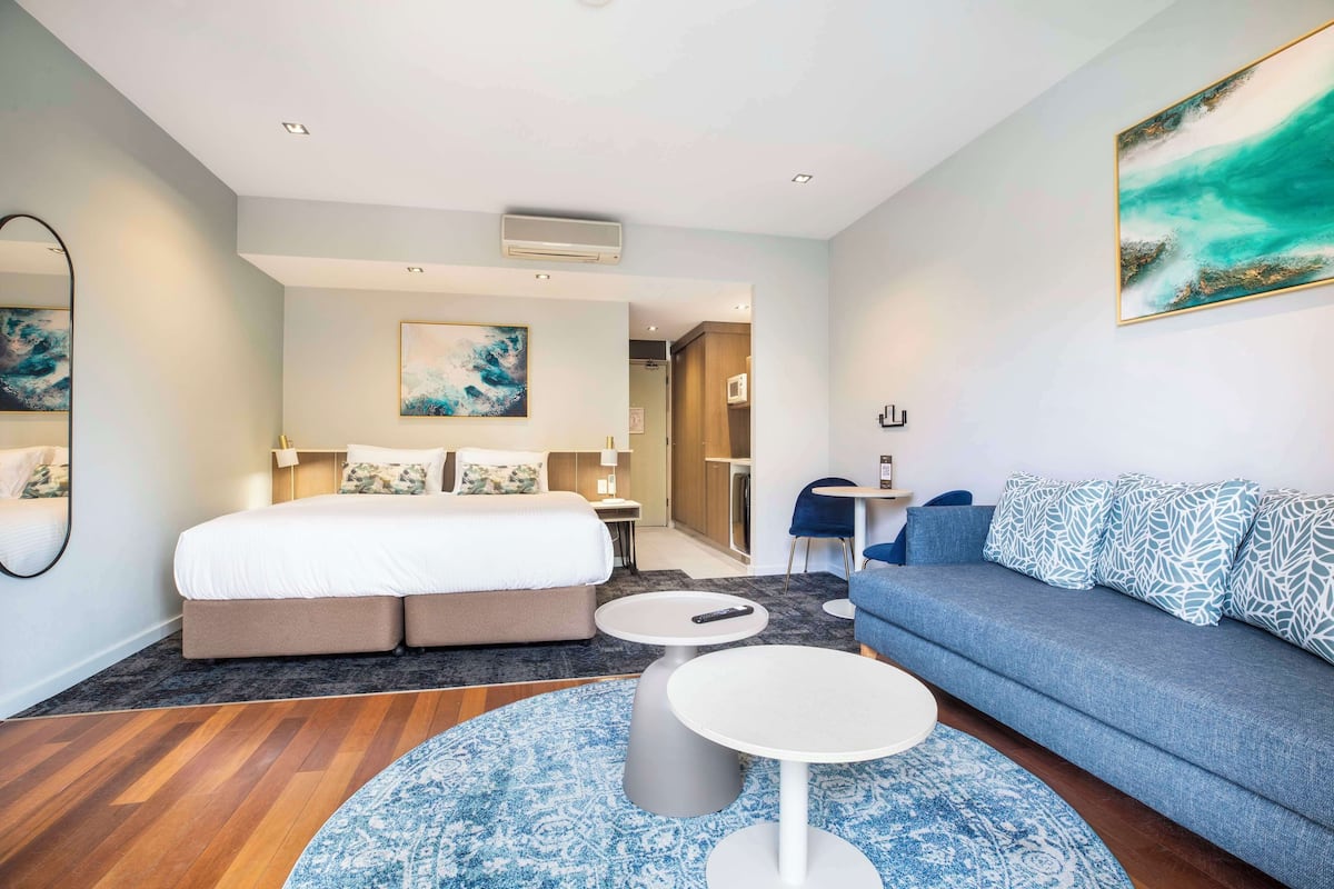 A modern hotel room with a bed, a sofa, a small table, and a large painting.