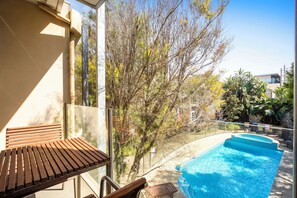 A poolside area with a wooden bench, a clear view of the pool, and surrounding trees.