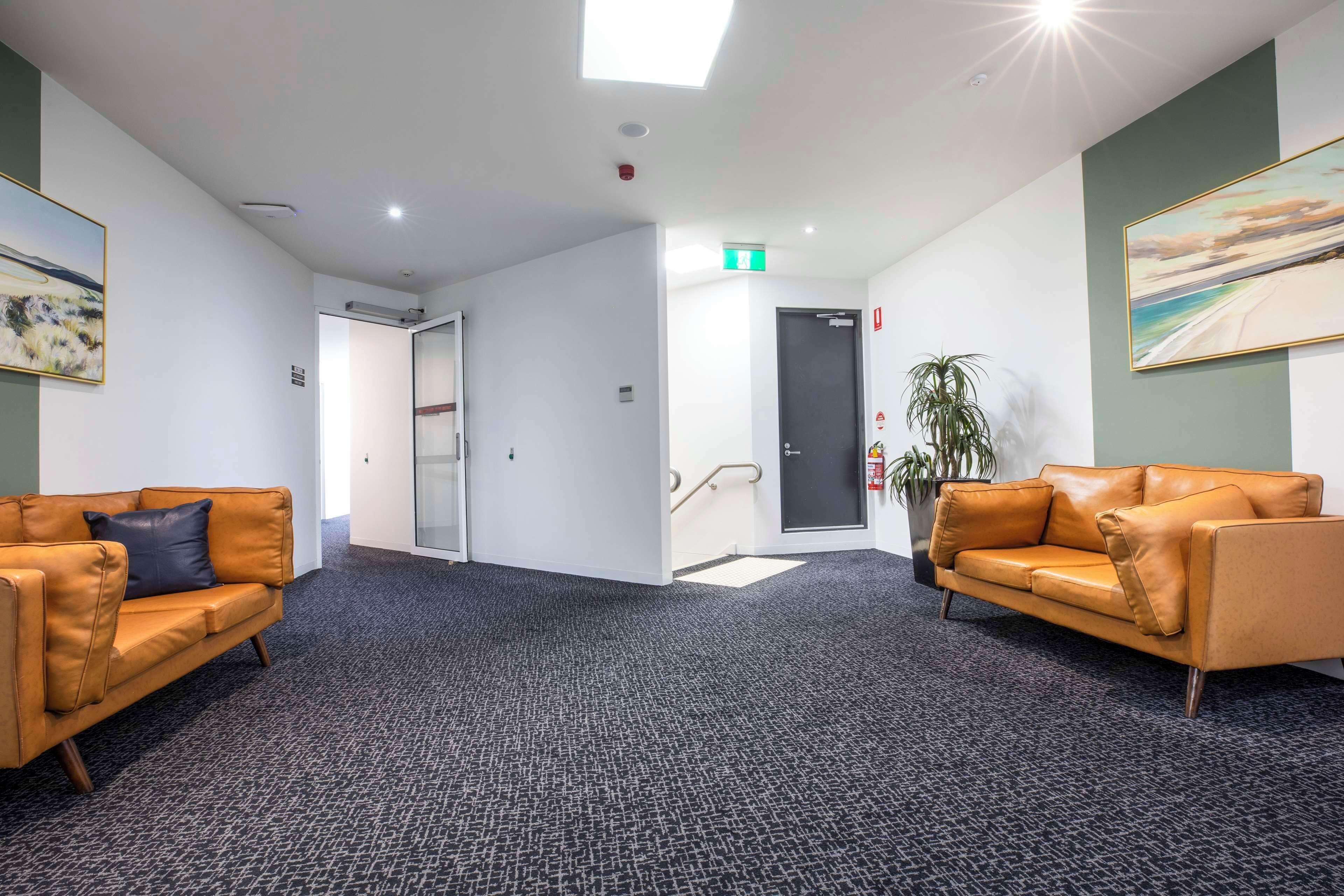 A modern lobby with two leather sofas, a patterned carpet, and a painting on the wall.