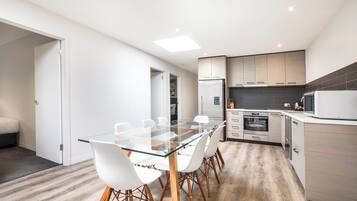 Una cocina moderna con una mesa de vidrio, sillas blancas y piso de madera.