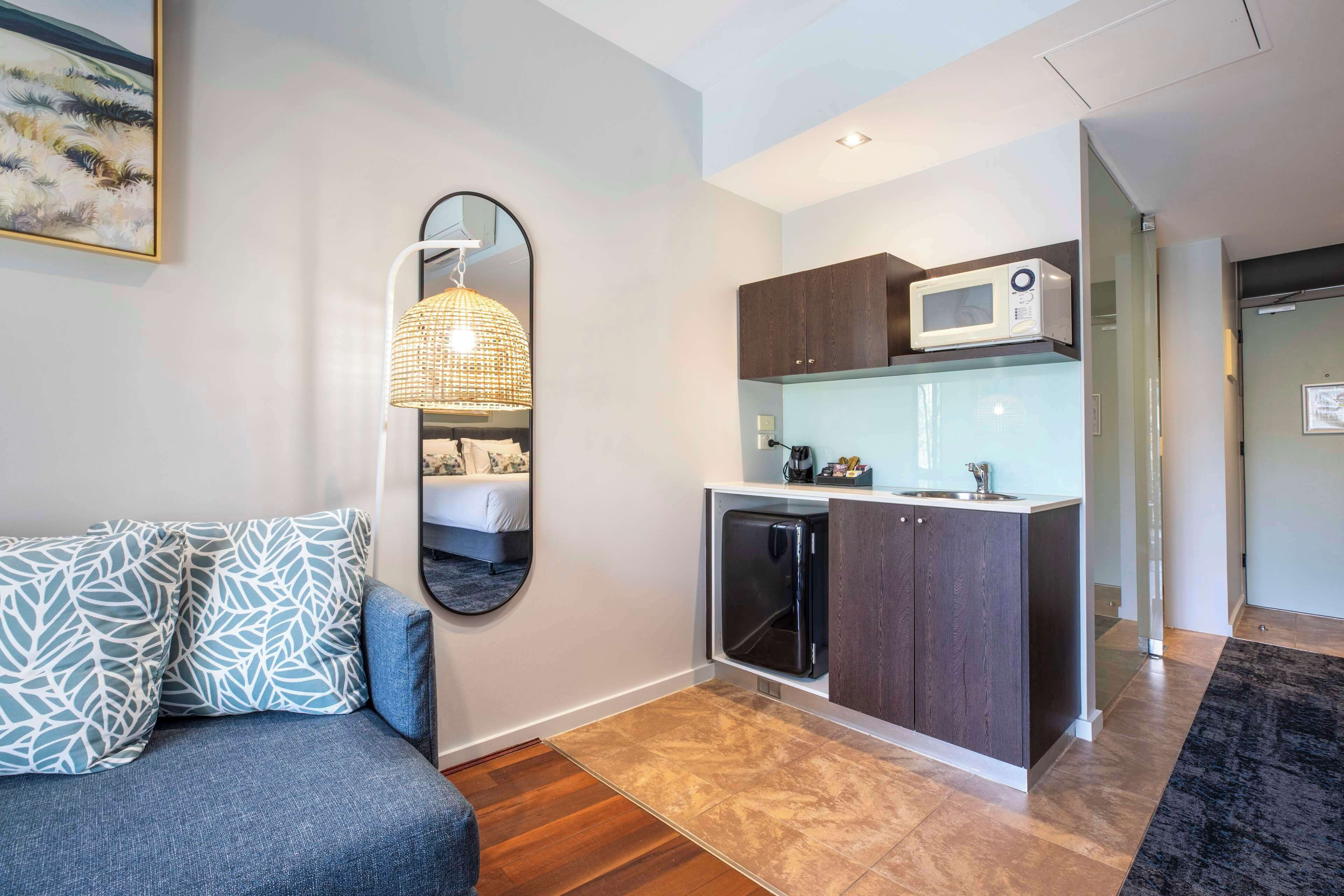 A compact living space with a kitchenette, a sofa with patterned cushions, and a large mirror.