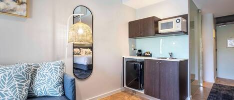 A compact living space with a kitchenette, a sofa with patterned cushions, and a large mirror.