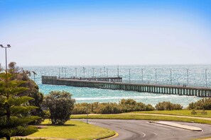 A coastal road with a view of a long pier extending into the sea.