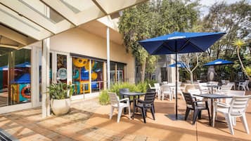 Un patio al aire libre con mesas, sillas, sombrillas y plantas en macetas.