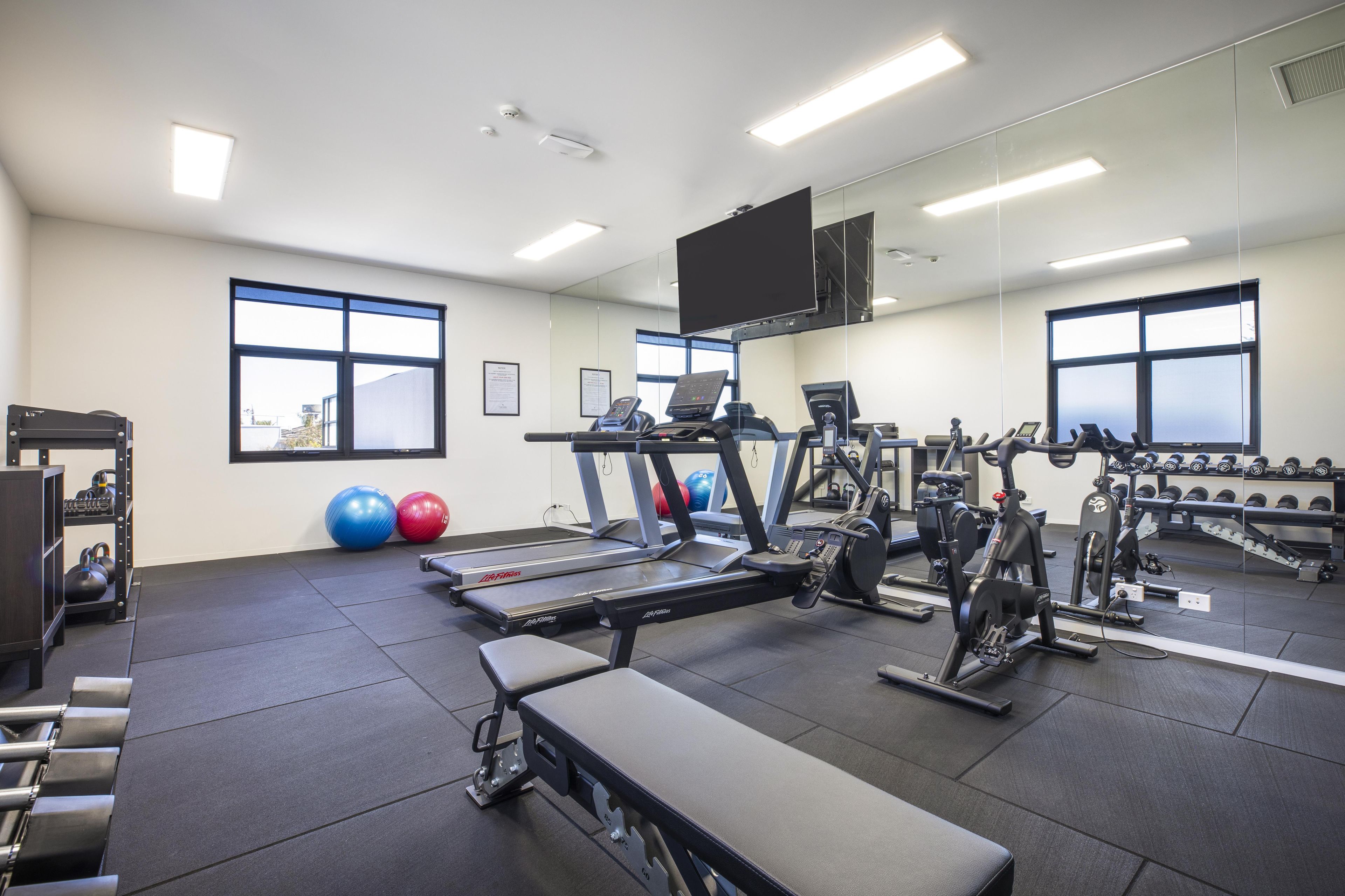 A gym with treadmills, elliptical machines, a bench, and exercise balls.