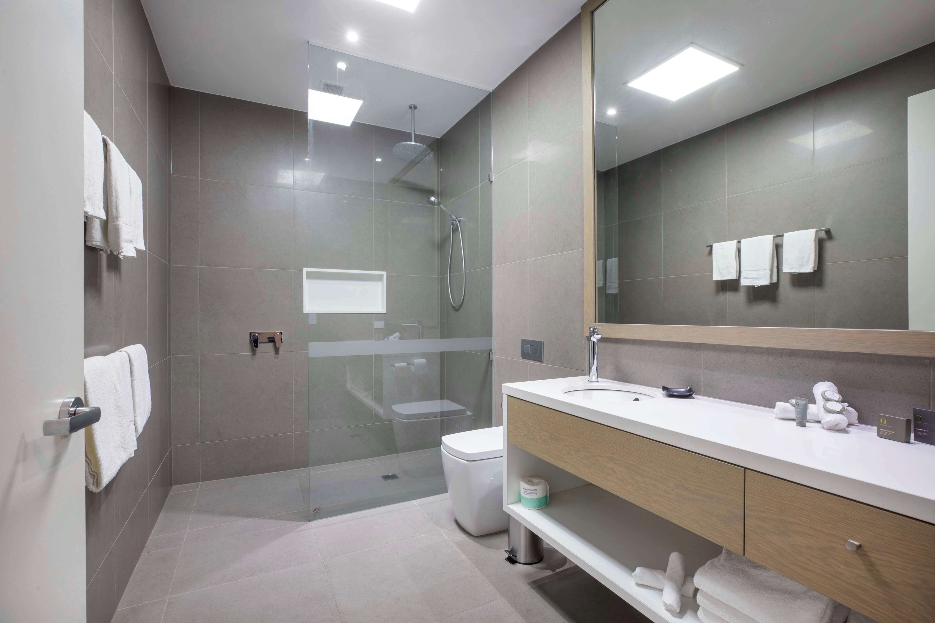 A modern bathroom with a glass-enclosed shower, a toilet, and a vanity with a mirror.