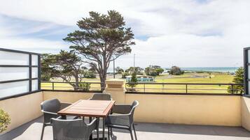 A balcony with a table and chairs, overlooking a golf course and the sea.
