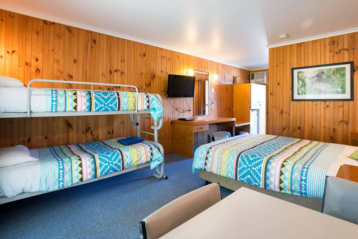Ein Schlafraum mit Etagenbett, Schreibtisch und einem Bett mit gemusterten Bettwaren.