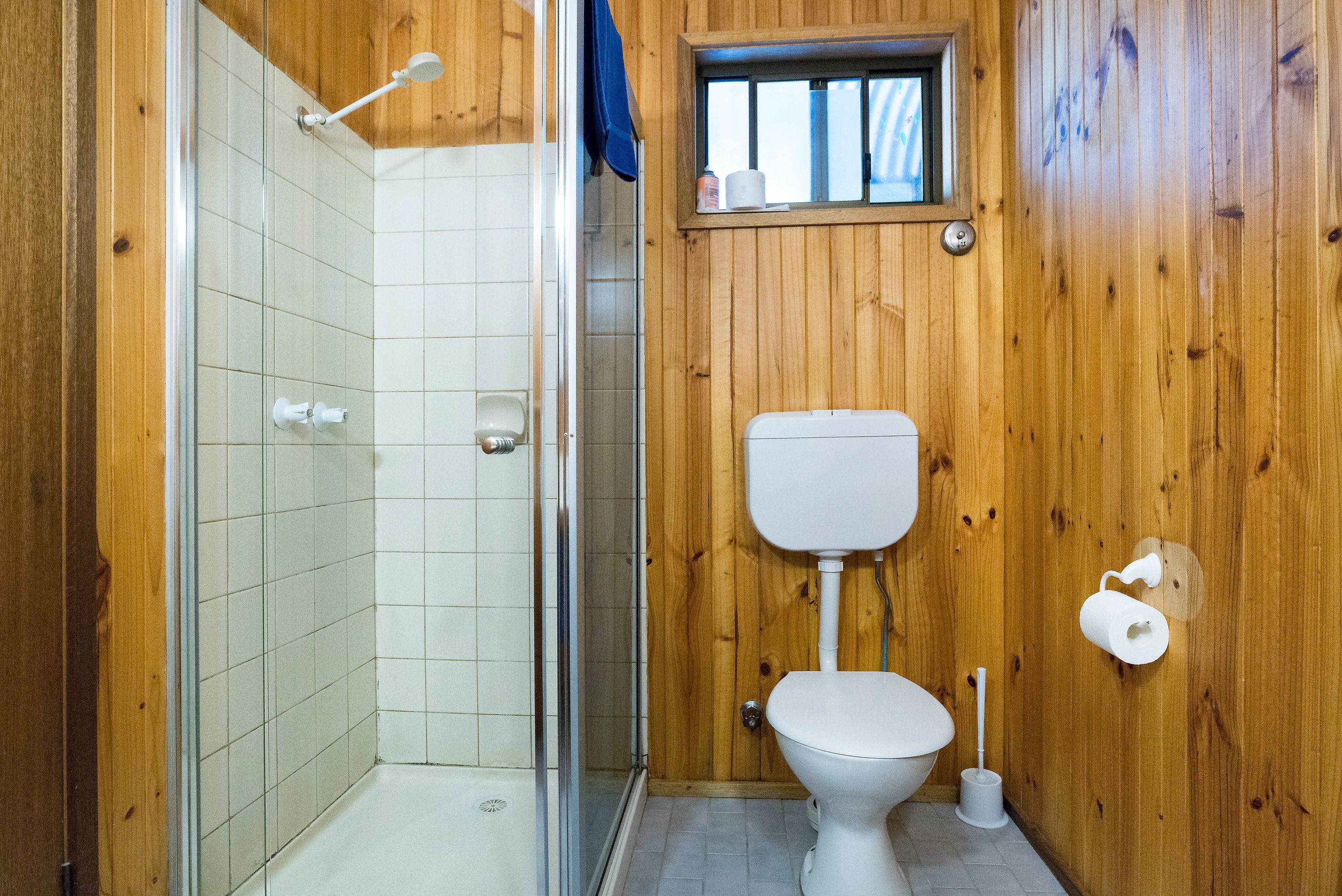Ein Badezimmer mit Dusche, Toilette und einem kleinen Fenster.