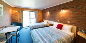 A room with two beds, a desk, and a chair. There is a brick wall and a wooden door. - Kookaburra Motor Lodge (Halls Gap)