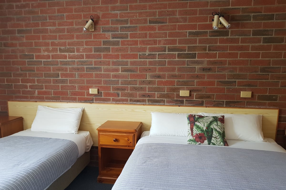 Ein Hotelzimmer mit zwei Einzelbetten, einem Holfnachtkästchen und einer Ziegelwand.
