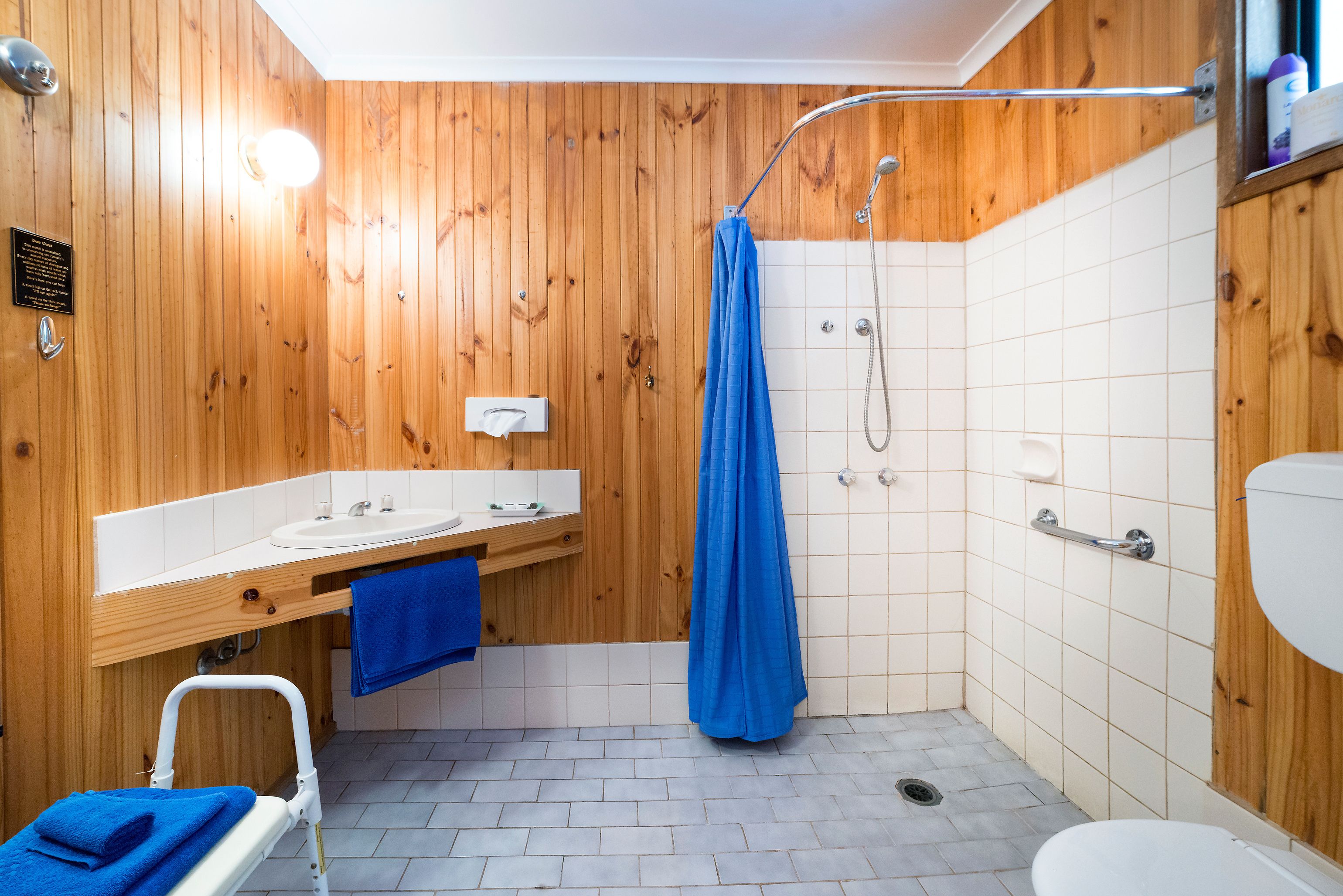 Ein Badezimmer mit Holzwandverkleidung, einer Dusche, einem Waschbecken und einer Toilette.